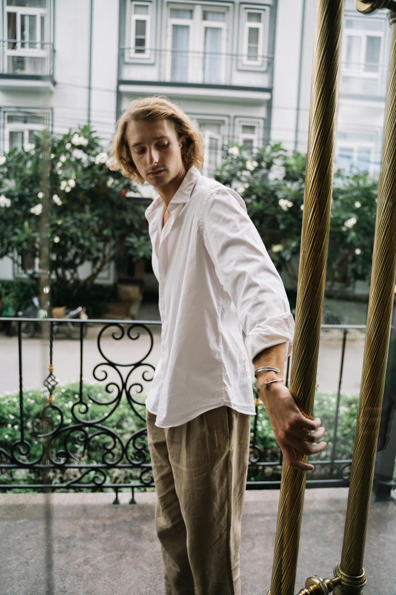 A man in casual fashion style stands outdoors holding a door, showcasing a relaxed and sophisticated look.